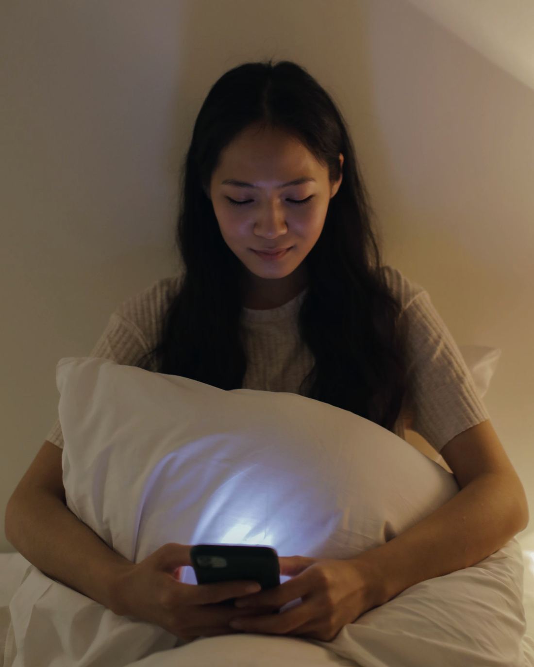 A young woman at night reading her phone, hugging a pillow