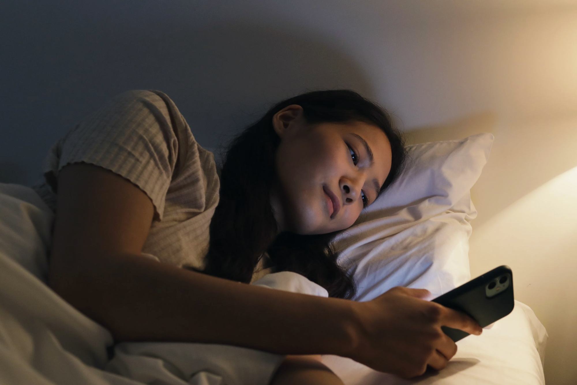 A young woman in bed at night, typing on her phone