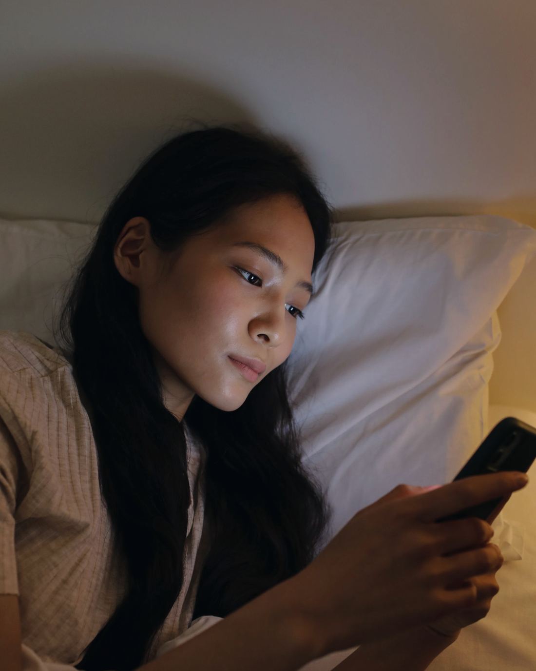 A young woman in bed reading a message on her phone