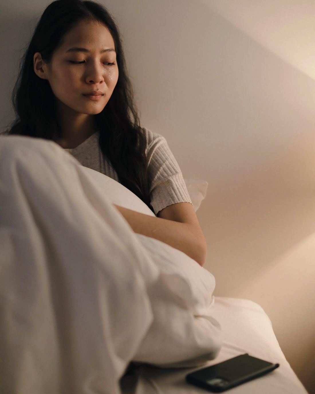 A young woman sitting on her bed, lost in thought, her phone beside her