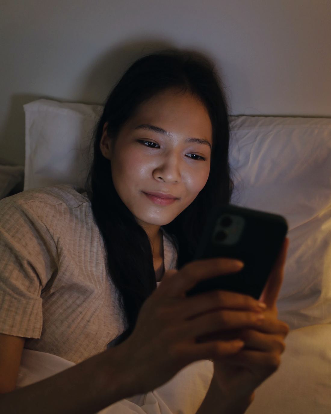 The same young woman smiles as she reads her phone